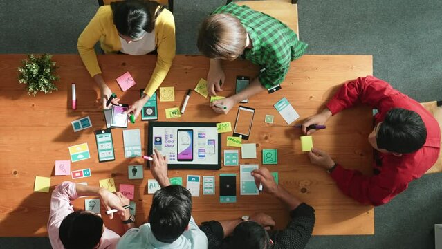 Programmer sharing Ux Ui design for mobile phone interface idea with software developer while designer writing idea at sticky notes. Start up team develop wireframe prototype. Time lapse. Convocation.