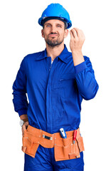 Young handsome man wearing worker uniform and hardhat confused and annoyed with open palm showing copy space and pointing finger to forehead. think about it.