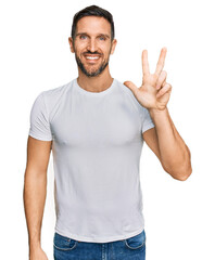 Handsome man with beard wearing casual white t shirt showing and pointing up with fingers number...
