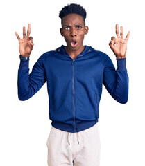 Young african american man wearing sportswear looking surprised and shocked doing ok approval symbol with fingers. crazy expression