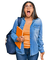 Young latin girl wearing student backpack and holding books angry and mad screaming frustrated and...