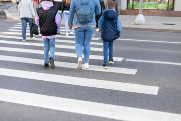 Urban life, safety of the urban environment. An unrecognizable family in casual clothes crosses the street at a pedestrian crossing. Group of people walking on the crosswalk