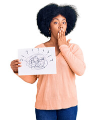 Young african american girl holding scribble draw covering mouth with hand, shocked and afraid for...