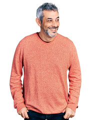 Middle age hispanic with grey hair wearing casual sweater looking away to side with smile on face,...