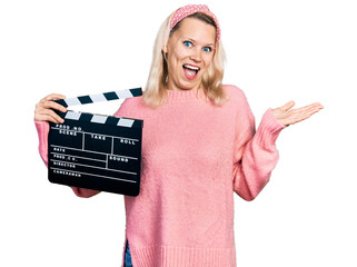 Young caucasian woman holding video film clapboard celebrating achievement with happy smile and...