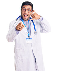 Young hispanic man wearing doctor uniform and stethoscope smiling doing talking on the telephone...