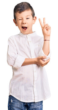 Cute blond kid wearing elegant shirt smiling with happy face winking at the camera doing victory sign with fingers. number two.