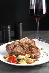 Delicious fried beef meat, vegetables and glass of wine on grey table