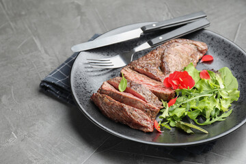 Delicious grilled beef meat served with greens on grey table