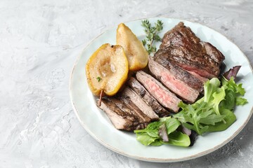 Pieces of delicious roasted beef meat, caramelized pear and greens on light textured table. Space for text