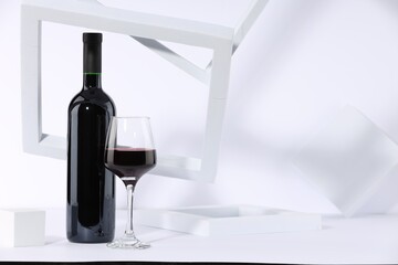 Stylish presentation of delicious red wine in bottle and glass on white background. Space for text