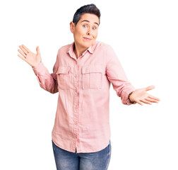 Young woman with short hair wearing casual clothes clueless and confused expression with arms and...