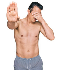 Fototapeta premium Handsome young man wearing swimwear shirtless covering eyes with hands and doing stop gesture with sad and fear expression. embarrassed and negative concept.