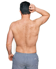 Fototapeta premium Handsome young man wearing swimwear shirtless backwards thinking about doubt with hand on head