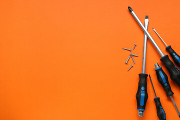 Set of screwdrivers and screws on orange background, flat lay. Space for text