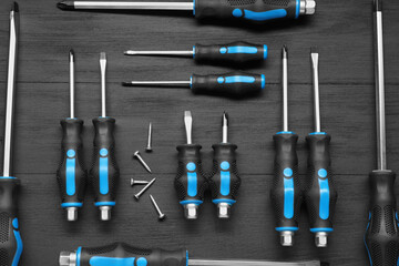 Set of screwdrivers and screws on black wooden table, flat lay