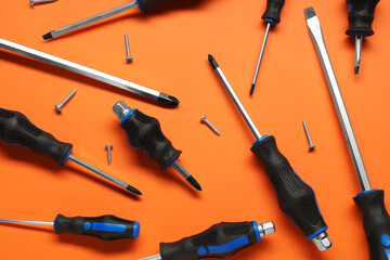 Set of screwdrivers and screws on orange background, flat lay