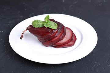 Tasty red wine poached pear and mint on black table, closeup