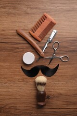 Artificial moustache and barber tools on wooden table, flat lay