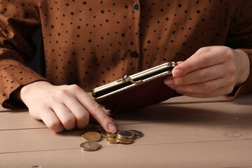 Poverty. Woman with wallet counting coins at wooden table, closeup - obrazy, fototapety, plakaty