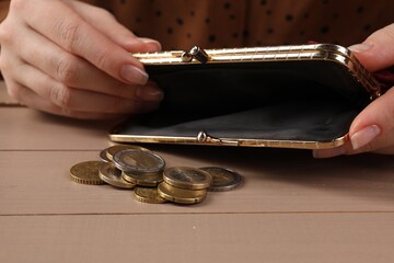 Poverty. Woman with empty wallet and coins at wooden table, closeup