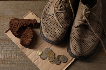 Poverty. Old shoes, coins, pieces of bread and cardboard sheet on wooden table, above view - obrazy, fototapety, plakaty