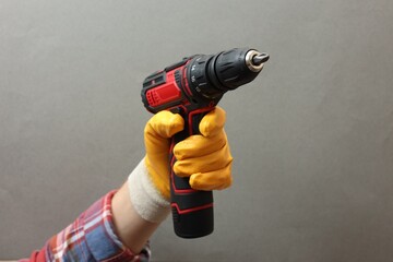 Handyman holding electric screwdriver on grey background, closeup - obrazy, fototapety, plakaty