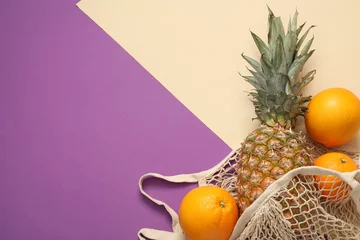 Foto op Plexiglas String bag with fresh pineapple and oranges on color background, flat lay. Space for text © New Africa