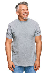 Middle age grey-haired man wearing casual clothes looking away to side with smile on face, natural expression. laughing confident.