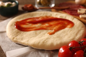 Pizza dough with tomato sauce and products on table, closeup