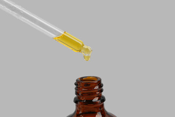 Dripping tincture from pipette into bottle on white background