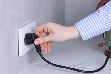 Woman plugging electric kettle into power socket at white table indoors, closeup