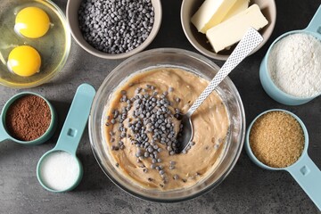 Raw dough with chocolate chips in bowl and ingredients on grey table, flat lay