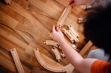 Hands carefully piece together curves of a wooden railway track, crafting a journey on the rich,...