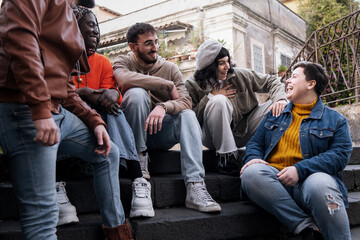 Group of multicultural friends sharing laughter and joy sitting on city steps - Young adults...