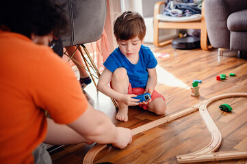 A young boy in blue concentrates on building a wooden toy train track on a hardwood floor, embodying childhood imagination and play