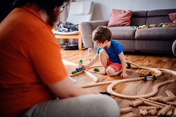 Engrossed in play, a young child sits on a wooden floor arranging a train track, highlighting a moment of creative engagement