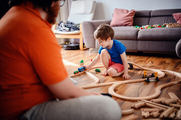 Engrossed in play, a young child sits on a wooden floor arranging a train track, highlighting a...