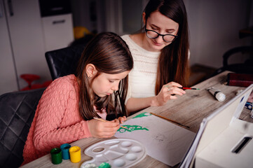 A girl and an adult woman focus intently on painting, a shared creative activity at a home...