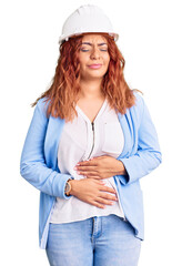 Young latin woman wearing architect hardhat with hand on stomach because indigestion, painful illness feeling unwell. ache concept.