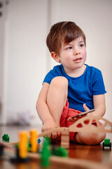 A joyful young boy with a smartphone sits amidst a wooden train setup, his bright laughter echoing...