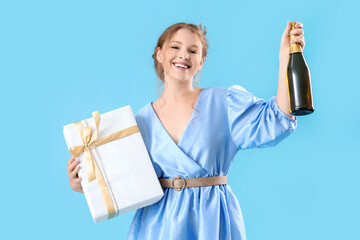 Beautiful woman with Birthday gift and bottle of champagne on light blue background