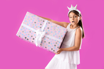 Surprised little girl with Birthday gift box on purple background