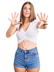 Young beautiful blonde woman wearing casual white tshirt afraid and terrified with fear expression stop gesture with hands, shouting in shock. panic concept.