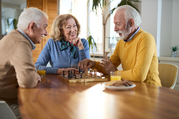 Group of happy seniors talking while playing chess  at home.