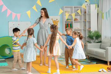 Little children with nursery teacher doing round dance in kindergarten