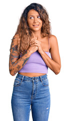 Fototapeta premium Young hispanic woman with tattoo wearing casual clothes laughing nervous and excited with hands on chin looking to the side