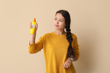 Beautiful young Asian woman with mosquito repellent spray on beige background
