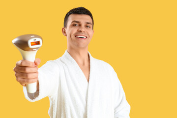 Young man with photoepilator on yellow background