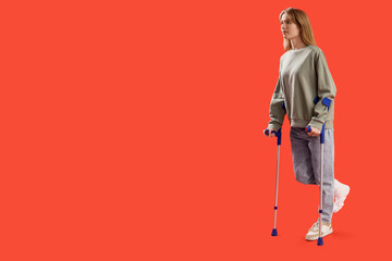 Injured young woman after accident with broken foot and crutches on red background